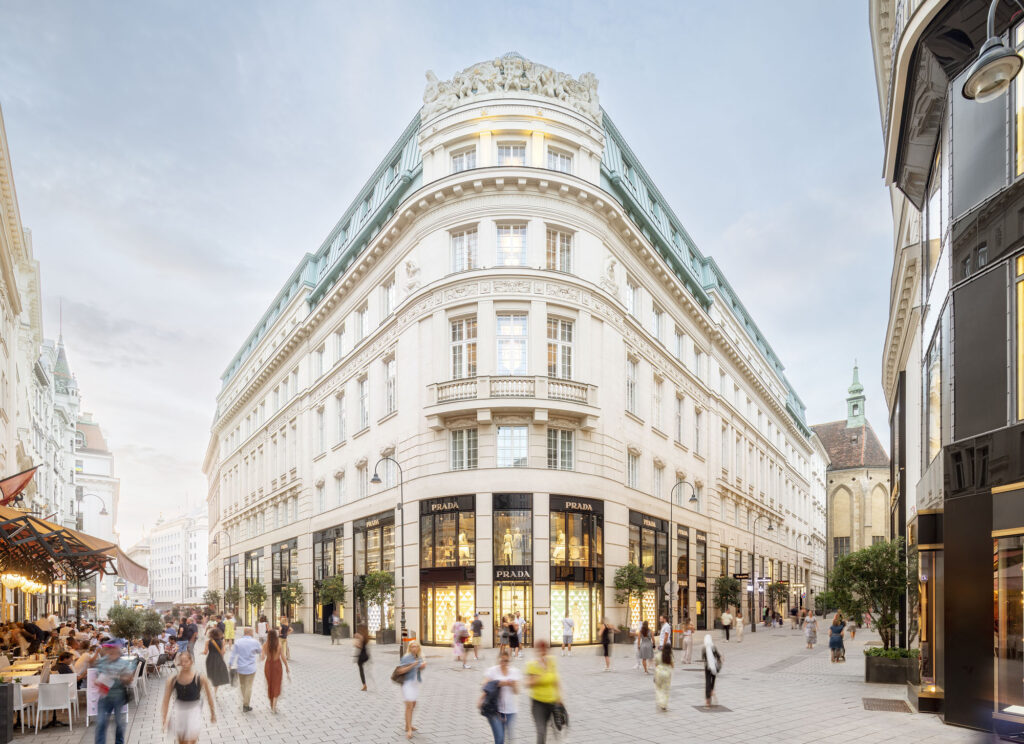 Elegant historic corner building on a busy square with pedestrians in front of large storefront windows.