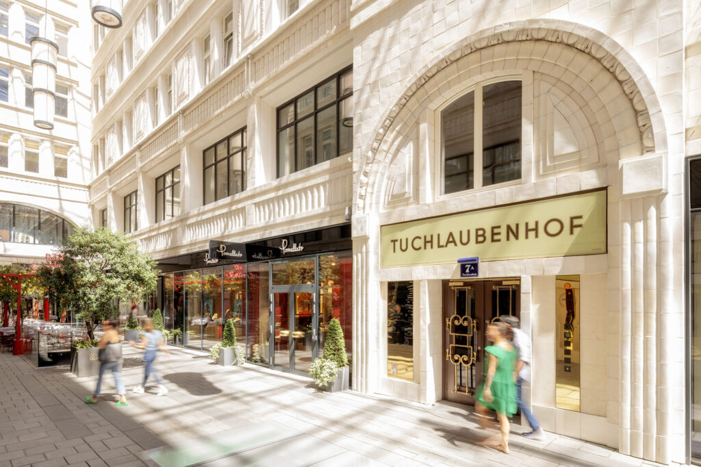 Entrance to the Tuchlaubenhof arcade with arched architecture, shop windows, and passersby.